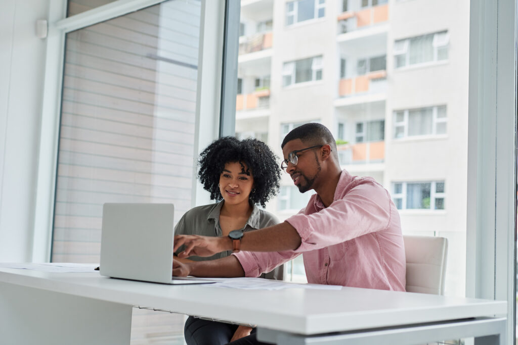 Two young black professionals working together to solve a problem on a laptop in a downtown office