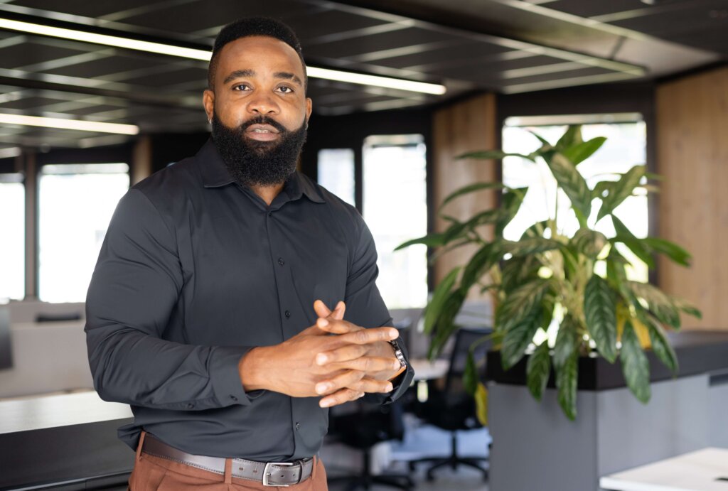 Black businessman in an office, standing by a plant