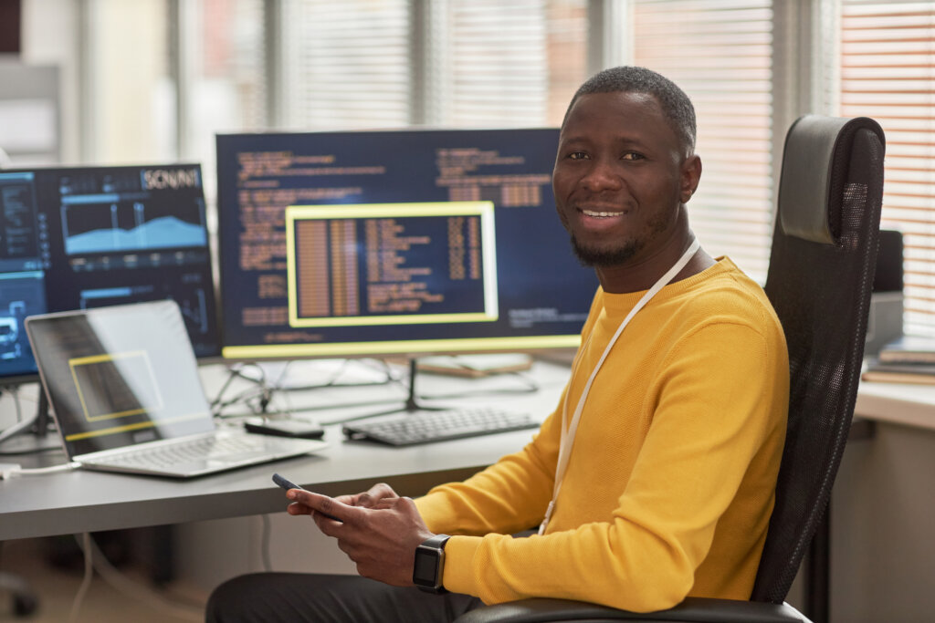 Smiling black man looking at camera at workplace in software development